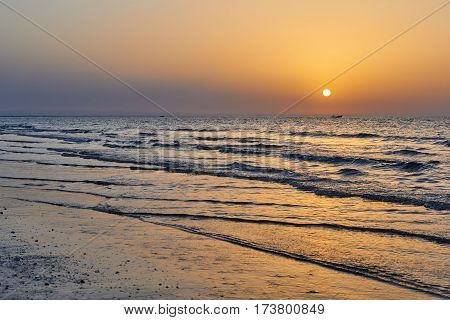 Beautiful golden sunset with the sun reflecting on the water and a row of fishing boats on the distant horizon