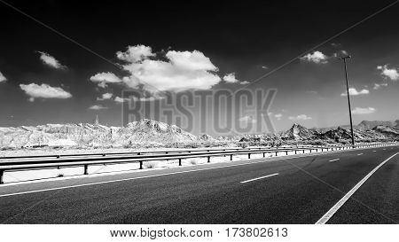 Infrared image of a asphalt road and a guardrail against a background of hills and a dark sky with clouds