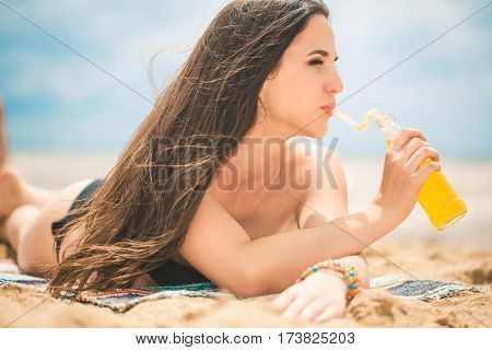 Beach woman drinking cold drink beverage having fun at beach party. Female babe in bikini enjoying orange water from glass boutle. summer concept