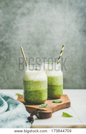 Ombre layered green smoothies with mint in glass jars with straws on wooden board, grey concrete wall background, copy space, selective focus. Clean eating, vegan, weight loss, healthy food concept