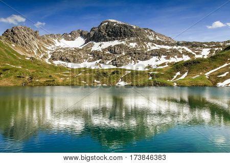 Beautiful reflections in the remote Schrecksee lake up high in the alpine mountains spotted with snow in spring or summer. Bavaria, Allgau, Germany.