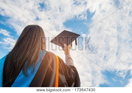 Graduates of the UniversityOf graduates holding hats handed to the sky.