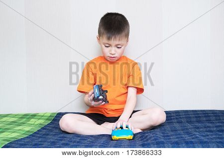 child playing car gameboy playing with toys sitting on bed indoorkid holding two toy cars at home alone