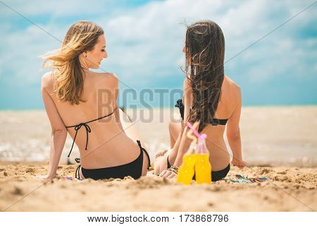 Gierlfriends drinking cold drink beverage having fun at beach party. Female babes in bikini enjoying orange water from glass boutle. summer concept