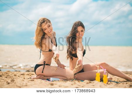 Gierlfriends drinking cold drink beverage having fun at beach party. Female babes in bikini enjoying orange water from glass boutle. summer concept