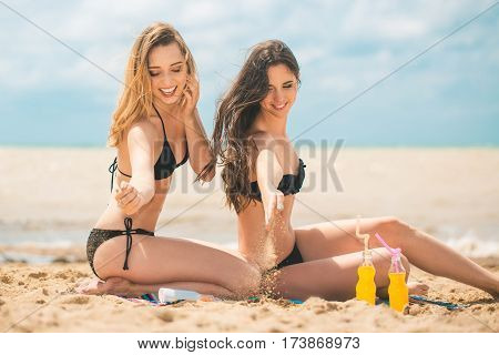 Gierlfriends drinking cold drink beverage having fun at beach party. Female babes in bikini enjoying orange water from glass boutle. summer concept