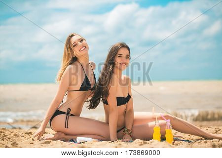 Gierlfriends drinking cold drink beverage having fun at beach party. Female babes in bikini enjoying orange water from glass boutle. summer concept