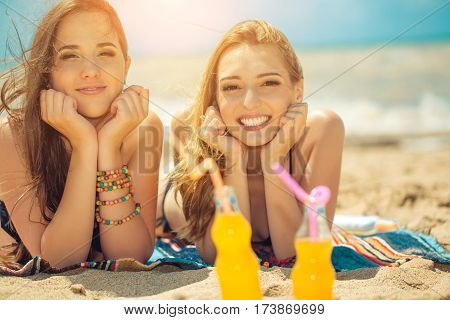 Gierlfriends drinking cold drink beverage having fun at beach party. Female babes in bikini enjoying orange water from glass boutle. summer concept