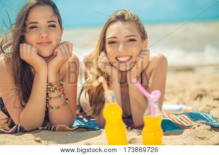 Gierlfriends drinking cold drink beverage having fun at beach party. Female babes in bikini enjoying orange water from glass boutle. summer concept
