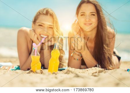 Gierlfriends drinking cold drink beverage having fun at beach party. Female babes in bikini enjoying orange water from glass boutle. summer concept