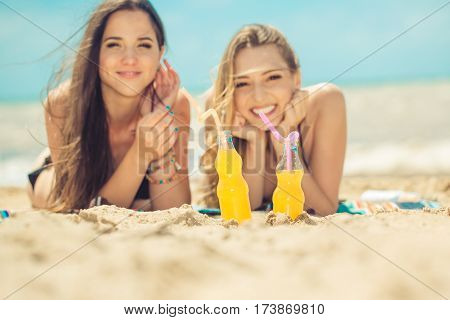 Gierlfriends drinking cold drink beverage having fun at beach party. Female babes in bikini enjoying orange water from glass boutle. summer concept