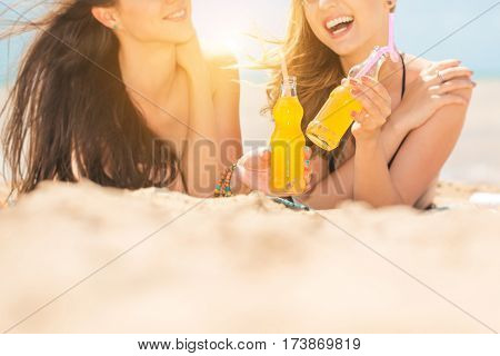 Gierlfriends drinking cold drink beverage having fun at beach party. Female babes in bikini enjoying orange water from glass boutle. summer concept