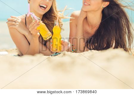 Gierlfriends drinking cold drink beverage having fun at beach party. Female babes in bikini enjoying orange water from glass boutle. summer concept