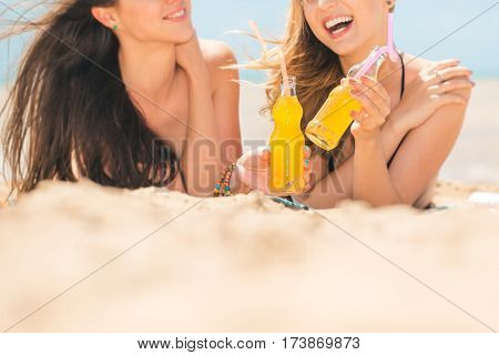Gierlfriends drinking cold drink beverage having fun at beach party. Female babes in bikini enjoying orange water from glass boutle. summer concept