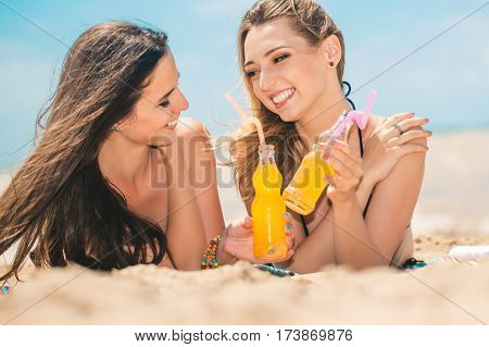 Gierlfriends drinking cold drink beverage having fun at beach party. Female babes in bikini enjoying orange water from glass boutle. summer concept
