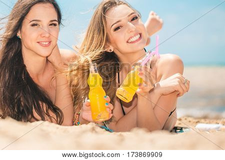 Gierlfriends drinking cold drink beverage having fun at beach party. Female babes in bikini enjoying orange water from glass boutle. summer concept
