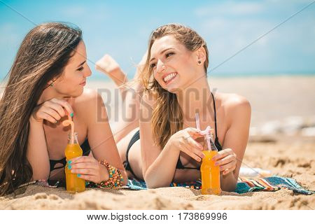 Gierlfriends drinking cold drink beverage having fun at beach party. Female babes in bikini enjoying orange water from glass boutle. summer concept