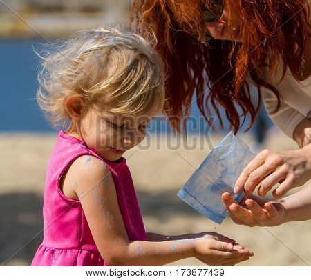 Adult woman pours out from the pack paint Holi to hands of a little girl.