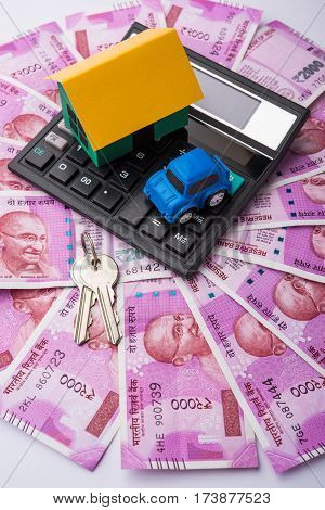 indian real estate or residential model house with new currency notes, keys, toy car and calculator, selective focus