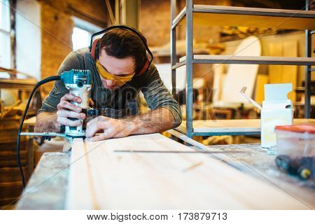 Professional joiner with wood-router cutting wooden plank