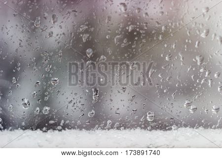 Background from a streams and drops of water on the window pane and strip of the wet snow at the bottom during a rain with sleet
