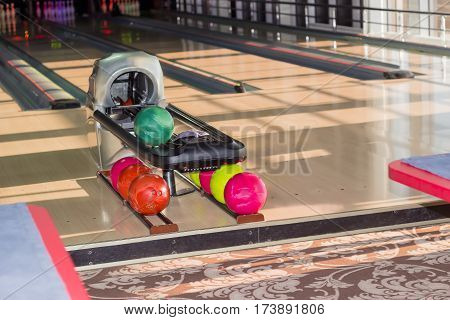 Playing area with several lanes with bowling pins and ball return device with colored bowling balls on the foreground in the modern pin bowling alley