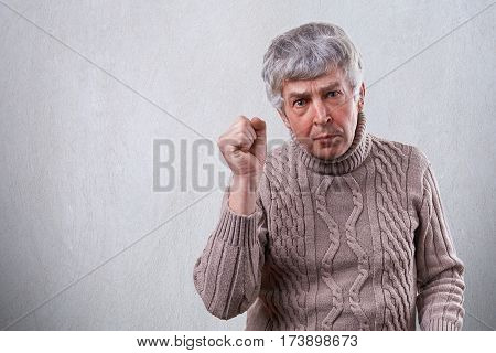 A handsome mature man showing his fist while being angry and irritated. A senior man with wrinkles showing his dissatisfaction with gesture. Facial expressions emotions feelings and people concept.