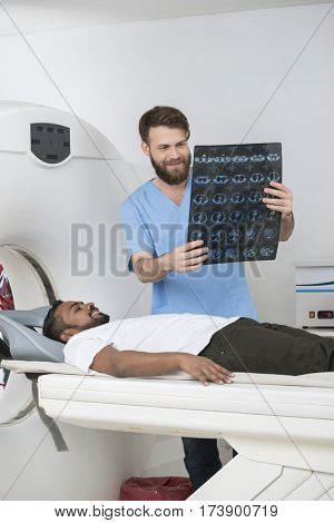 Radiologist Holding X-ray Report While Patient Lying On CT Scann