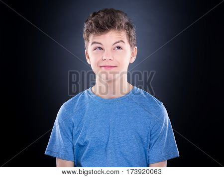 Casual thinking guy - caucasian male model. Half-length emotional portrait of teen boy wearing blue t-shirt. Thoughtful teenager, on black background. Handsome smart serious ponder child.