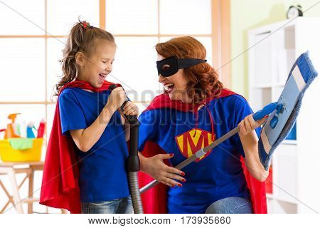 Happy woman and kid is preparing for room cleaning. Mother and her child girl playing together. Family in Superhero costumes.
