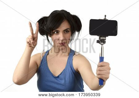 young attractive and sexy woman taking selfie photo with stick and mobile phone camera posing happy and playful peace sign isolated on white background in shooting self portrait