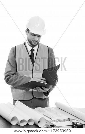 Building industry pro. Monochrome studio shot of a businessman builder in a protective helmet and safety vest working on his building plans making notes on clipboard architect worker engineer concept