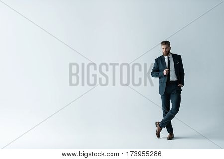 Full length view of handsome bearded businessman in stylish suit posing on grey