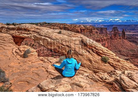 Young woman meditating at cliff by Mesa Arch. Canyonlands National Park. Moab. Utah. United States.