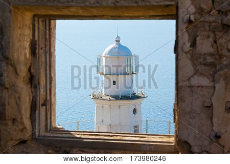 white lighthouse on the background of the sea in window of destroyed building