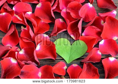 Valentines Day background: Heart shaped leaf and red rose petals on wooden background