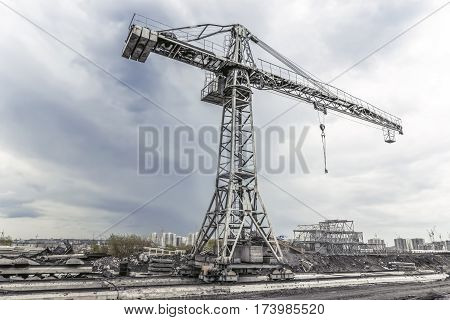 Grey building crane at the abandoned construction site in a cloudy day.