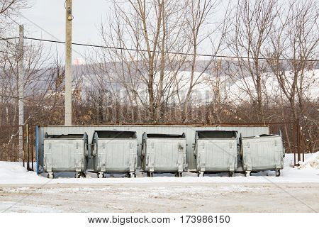 Five silver metal garbage containers in winter