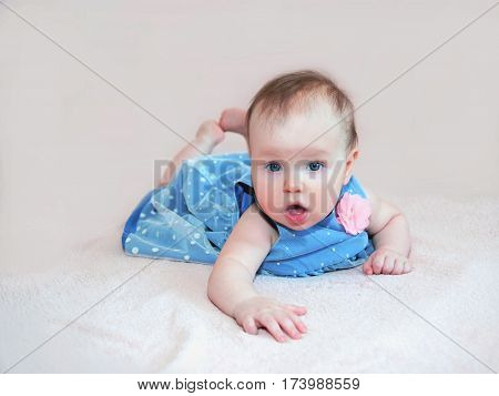baby girl in blue dress with pink flower lying and look smile