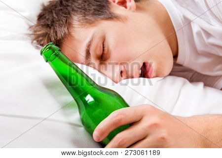 Young Man Sleep With A Beer Bottle In The Bed At The Home. Focus On The Bottle