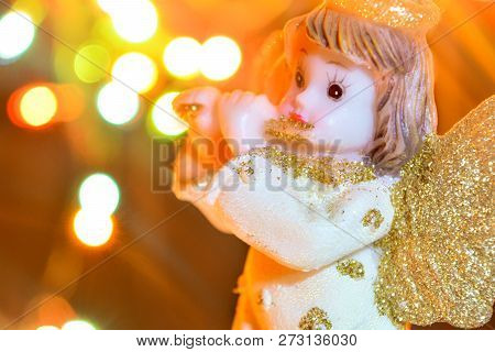 Figurine Of Little Angel With Golden Shiny Wings And Halo That Plays Flute On Shining Background Of 