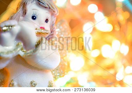 Figurine Of Little Angel With Golden Shiny Wings And Halo That Plays Flute On Shining Background Of 