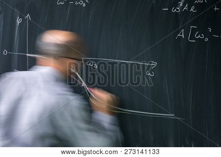 Math teacher drawing a fuction graph on a blackboard during mathclass (motion blurred image)