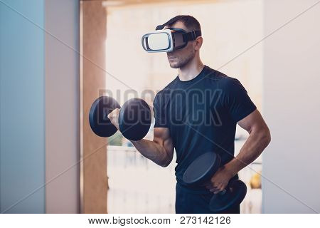Man Wearing Virtual Reality Glasses With Dumbbells. Athletic Man Performs An Exercise On The Strengt