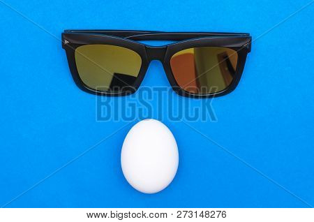 Chicken Egg And Sunglasses Above Isolated Ob A Blue Background.