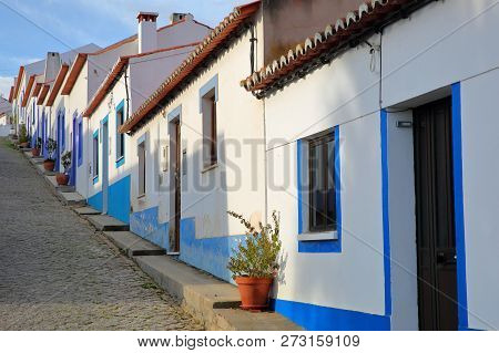 A Row Of Colorful Houses Along A Steep Cobbled Street Inside Odeceixe (near Aljezur), Leading To A W