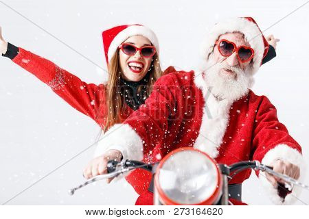 Santa Claus With White Beard Wearing Sungasses And Young Mrs. Claus Wearing Santa Hat, Red Sweater A