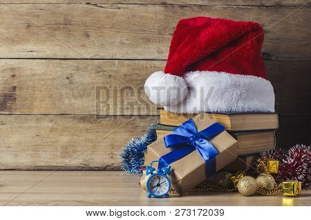 A Stack Of Books, Santa Clauss Cap, An Alarm Clock, Gift Boxes On A Wooden Background. Concept Of Ne