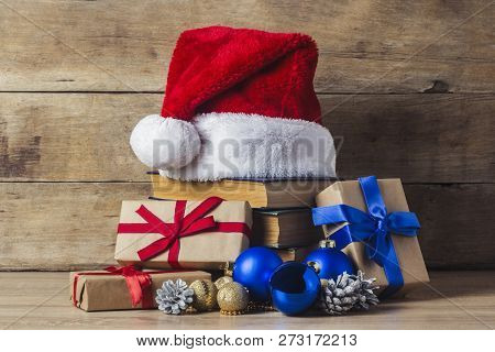 A Stack Of Books, Santa Clauss Cap, Cones, Christmas-tree Decorations, Gift Boxes On A Wooden Backgr