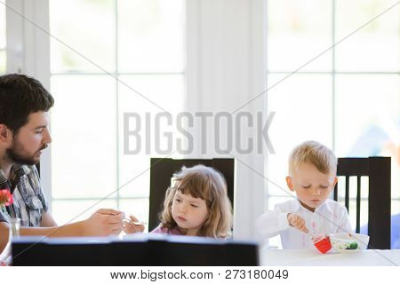 Father And His Two Little Childrens Eating Soup At The Kitchen At Home.